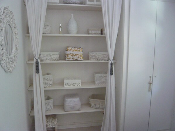 A white interior with a white wardrobe, shelves with baskets, and a decorative mirror. - Charming house located on the shore of Lake Maubuisson, close to the ocean. (Carcans)