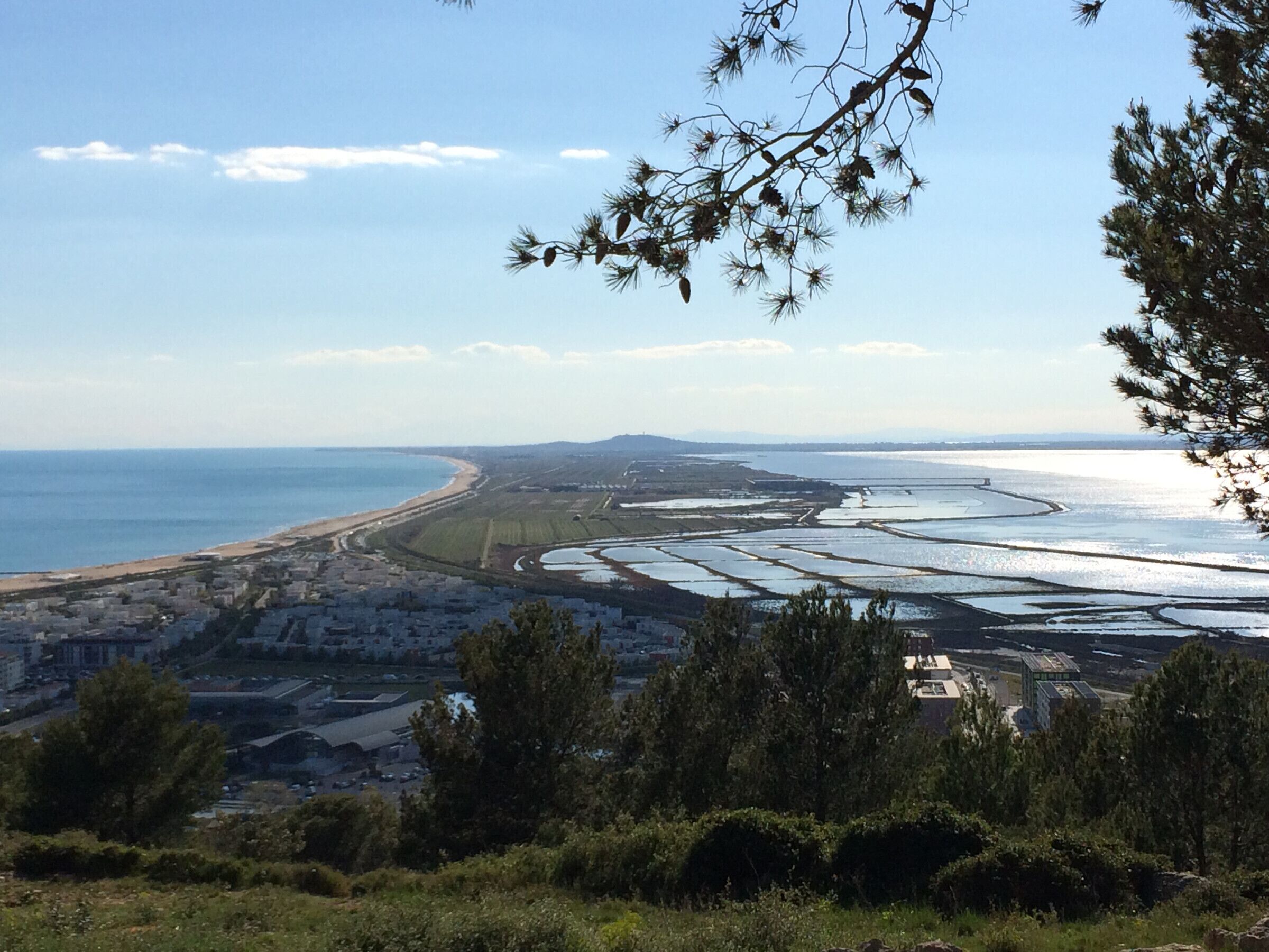 A coastal landscape with a beach, salt pans, and a city in the background.