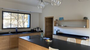 A modern kitchen with wooden cabinets, a black countertop, a large window, and pendant lights. - Bastide provençale 12 pers with swimming pool, 2 steps from Saint-Rémy-de-Pce (Eyragues)
