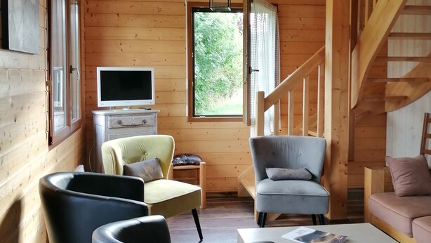 Ein gemütliches Blockhaus-Interieur mit Holzvertäfelung, einem Fernseher, einer Treppe und Sitzbereichen.