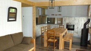 Ein gemütliches Wohnzimmer mit einer Holzsofa, einem Esstisch mit Stühlen und einer Küchenzeile mit Herd und Kaminofen.
