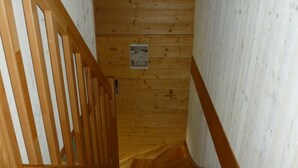 Eine Holztreppe mit Handlauf, die zu einem Raum mit weißer Wand und einem kleinen Fenster führt.