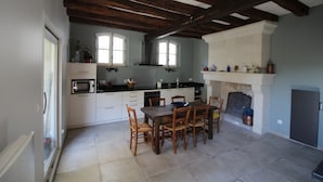 Una cocina con vigas de madera, una mesa de comedor con sillas, un microondas y una chimenea.