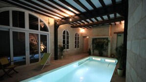 Una piscina interior con una pérgola, paredes de piedra y un área de descanso con sillas.