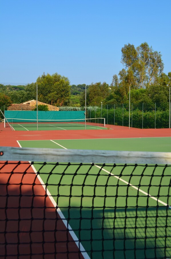 Ein Tennisplatz mit Netz, umgeben von Bäumen und einem Zaun.