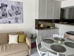 Een moderne keuken met witte kasten, een eettafel met grijze placemats en een beige bank met kussens.