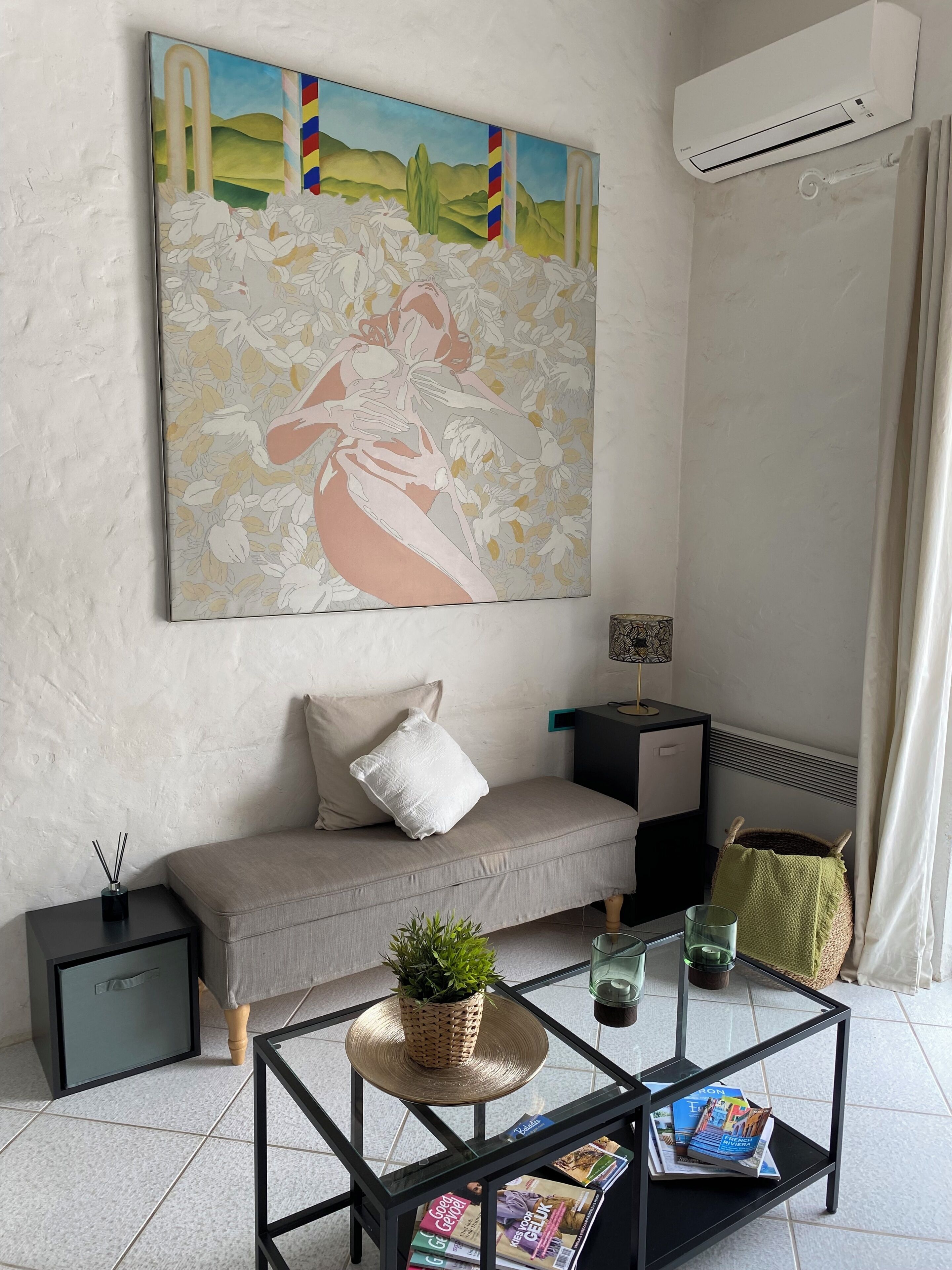 Een moderne woonkamer met een bank, een salontafel met tijdschriften, een schilderij aan de muur en een airconditioner.