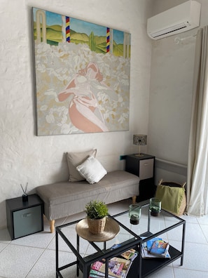 Een moderne woonkamer met een bank, een salontafel met tijdschriften, een schilderij aan de muur en een airconditioner.
