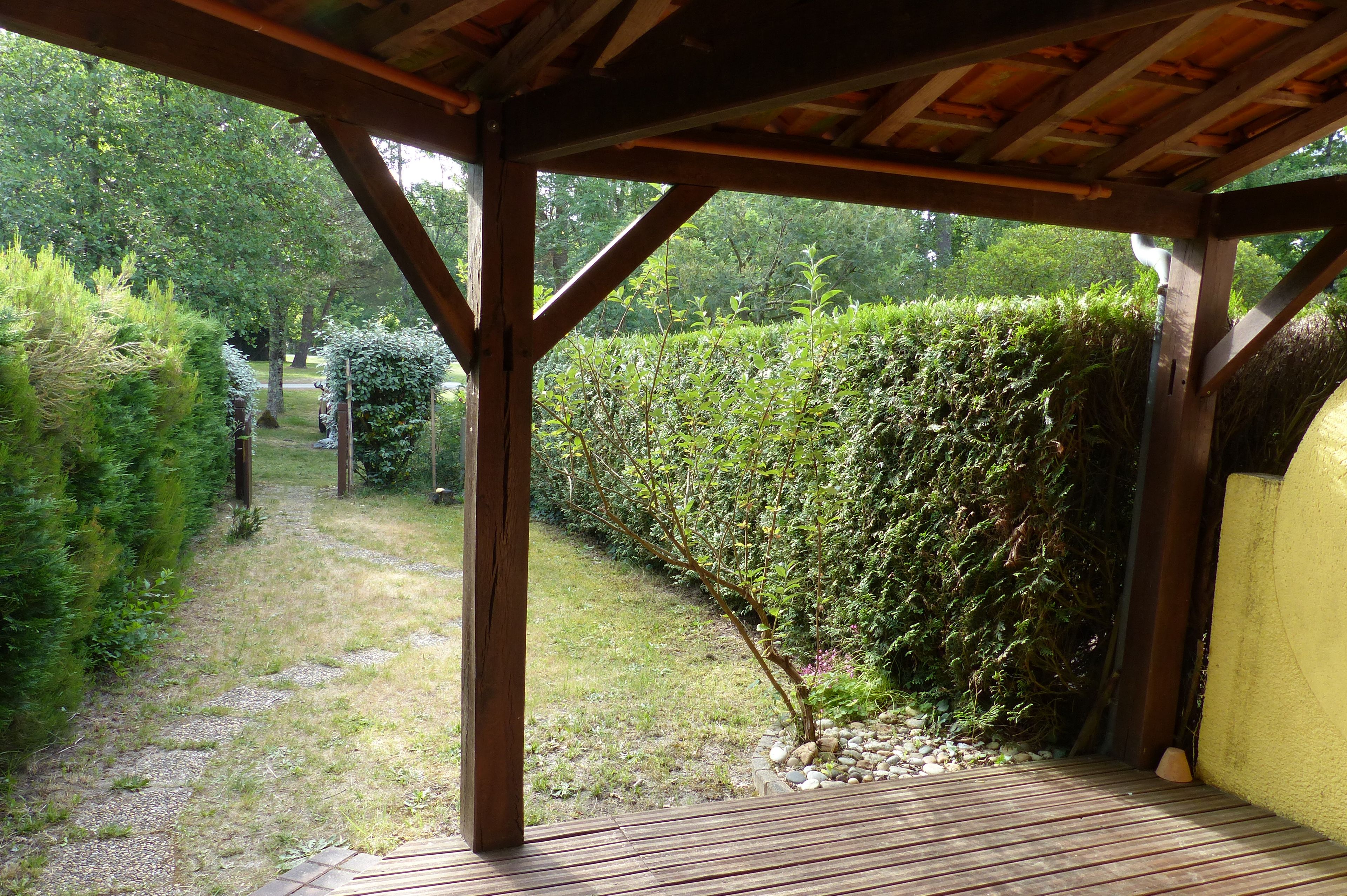 Una terraza de madera con vistas a un jardín y un seto.