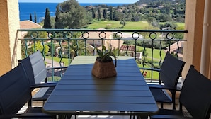 Een balkon met een tafel en stoelen, een bloempot en uitzicht op zee en heuvels.