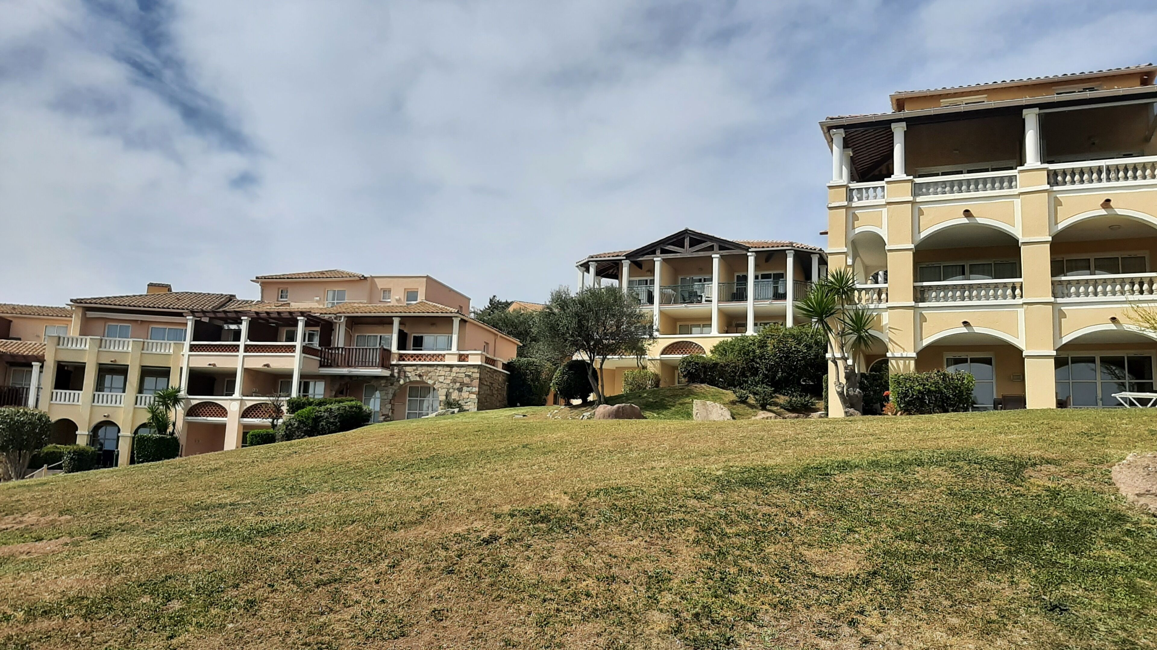 A residential area with multi-story buildings, a grassy hill, and a clear sky.