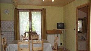 A dining area with a table and chairs, a television on a stand, and a window with curtains. - 1st floor apartment in Savoyard chalet in Morzine. (Morzine)
