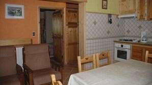 A room with a bed, a dining table, wooden chairs, a kitchen area with a stove and oven, and a tiled backsplash. - 1st floor apartment in Savoyard chalet in Morzine. (Morzine)