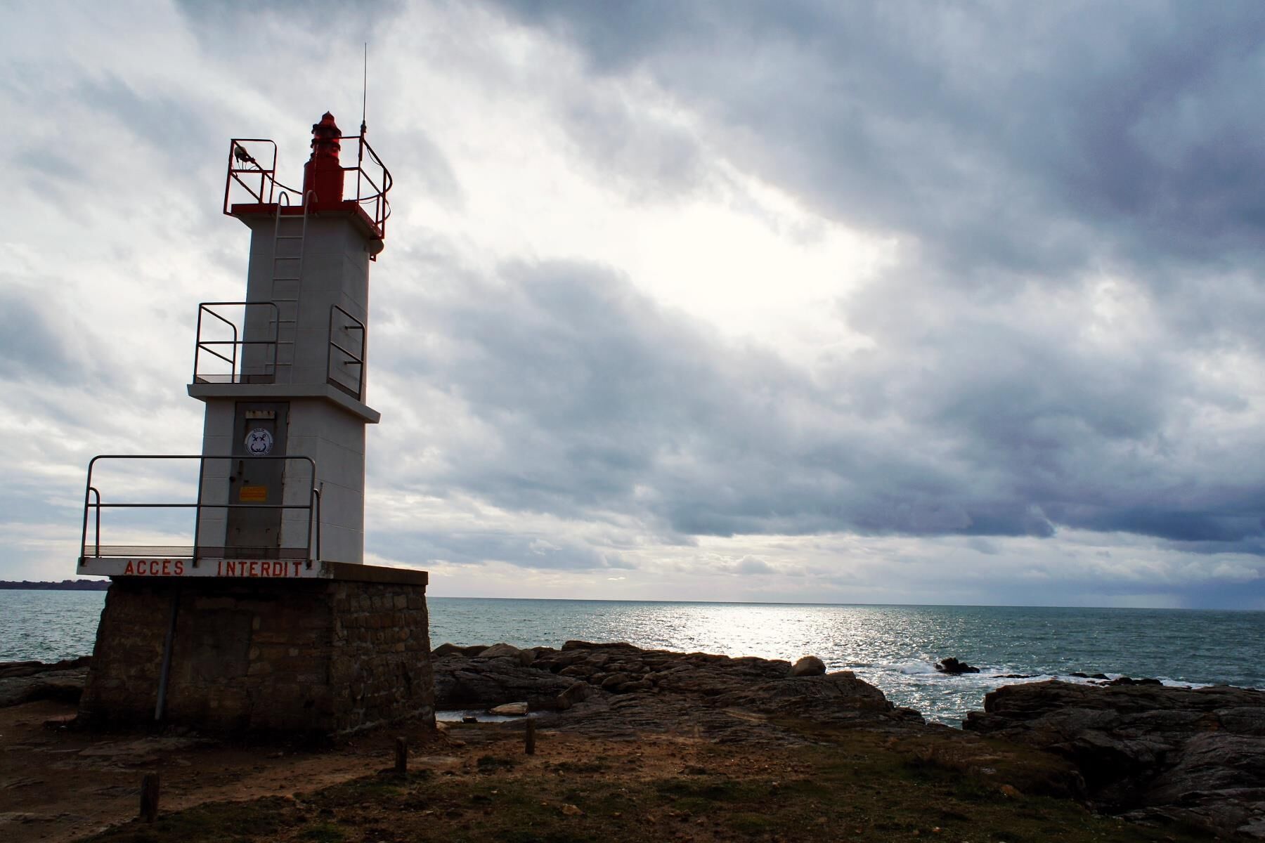 Un far amb base de pedra, barana metàl·lica i un senyal que diu "ACCES INTERDIT".