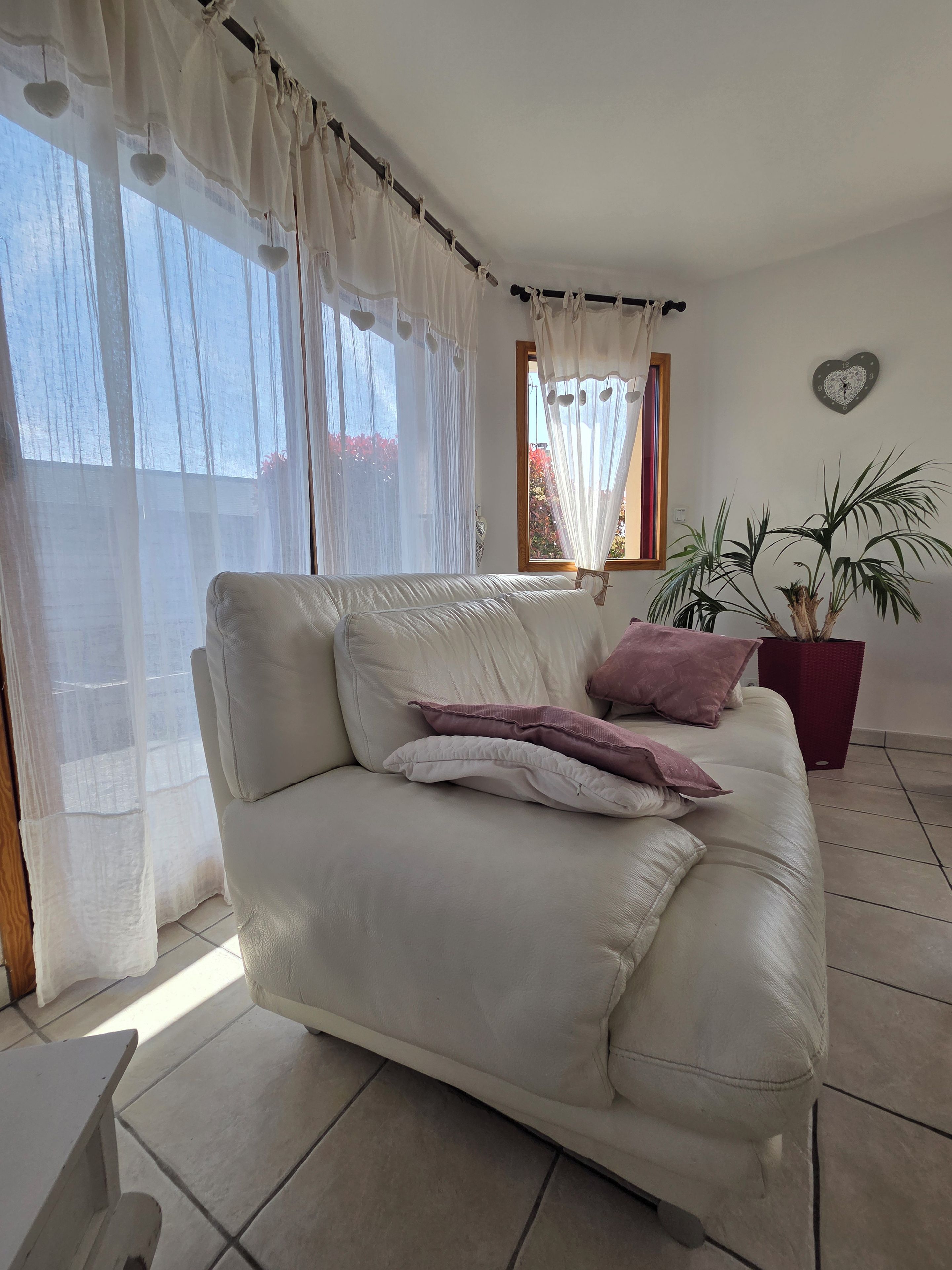 Una sala de estar con un sofá color beige, una planta en maceta y un reloj de pared.