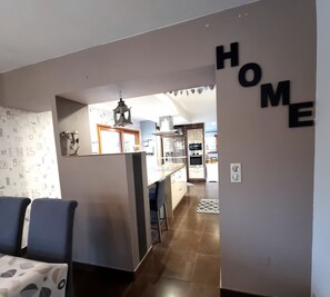 A modern kitchen with stainless steel appliances, a dining area with a patterned tablecloth, and a living room with a sofa. - Plénitude Bretonne: Indoor pool heated year-round, Jacuzzi, Sauna, Massage (Rédéné)