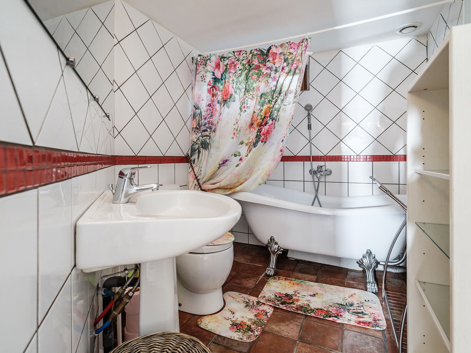 A bathroom with a white sink, toilet, and bathtub, tiled walls, and a floral shower curtain.