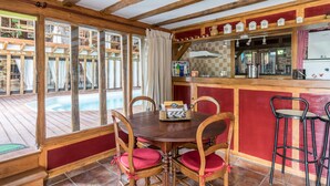 Une table à manger en bois avec quatre chaises, un coin bar avec des tabourets et une vue sur une piscine extérieure.