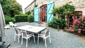 Un bâtiment en pierre avec une terrasse en gravier, une table et des chaises, et une porte bleue.