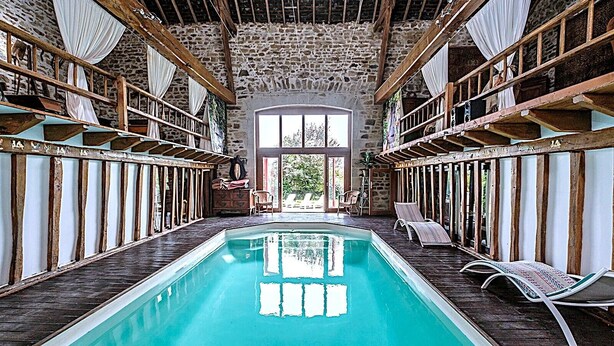 Une piscine dotée d’une terrasse en bois, de murs en pierre et offrant une vue sur l’extérieur.