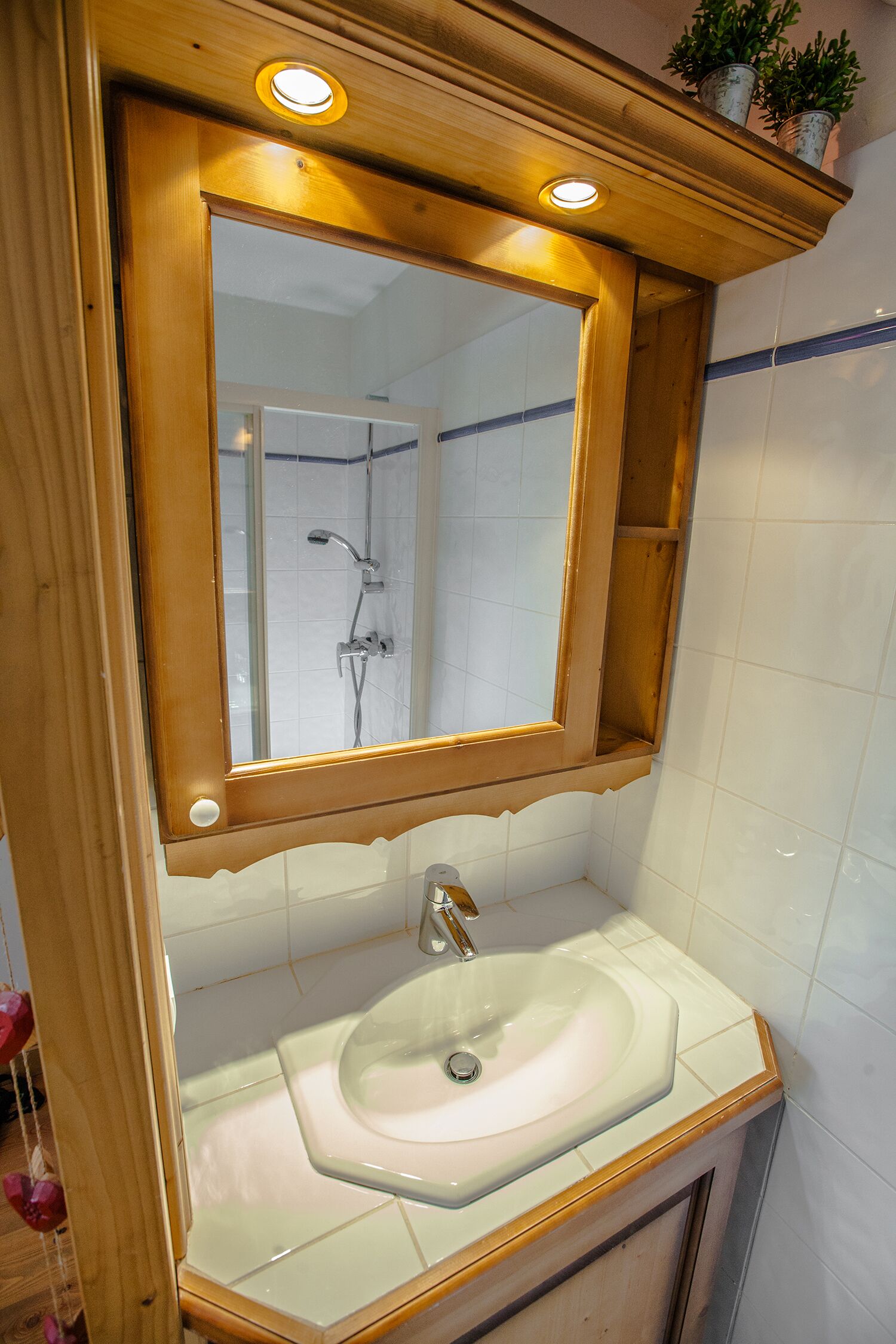 Une salle de bain avec un miroir à cadre en bois, un lavabo blanc et une douche visible à travers le miroir.