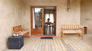 Une terrasse en bois avec un banc, une table entourée de chaises et une porte donnant sur un espace extérieur.