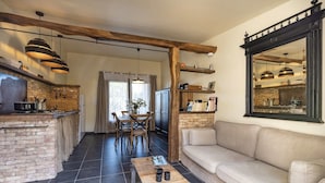 Un salon chaleureux avec un canapé et une table basse, une cuisine avec un mur en briques et des poutres en bois, et un coin repas avec une table et des chaises.