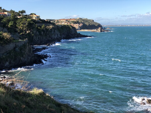 Paisaje costero con acantilados rocosos, mar azul cristalino y edificios en la ladera.