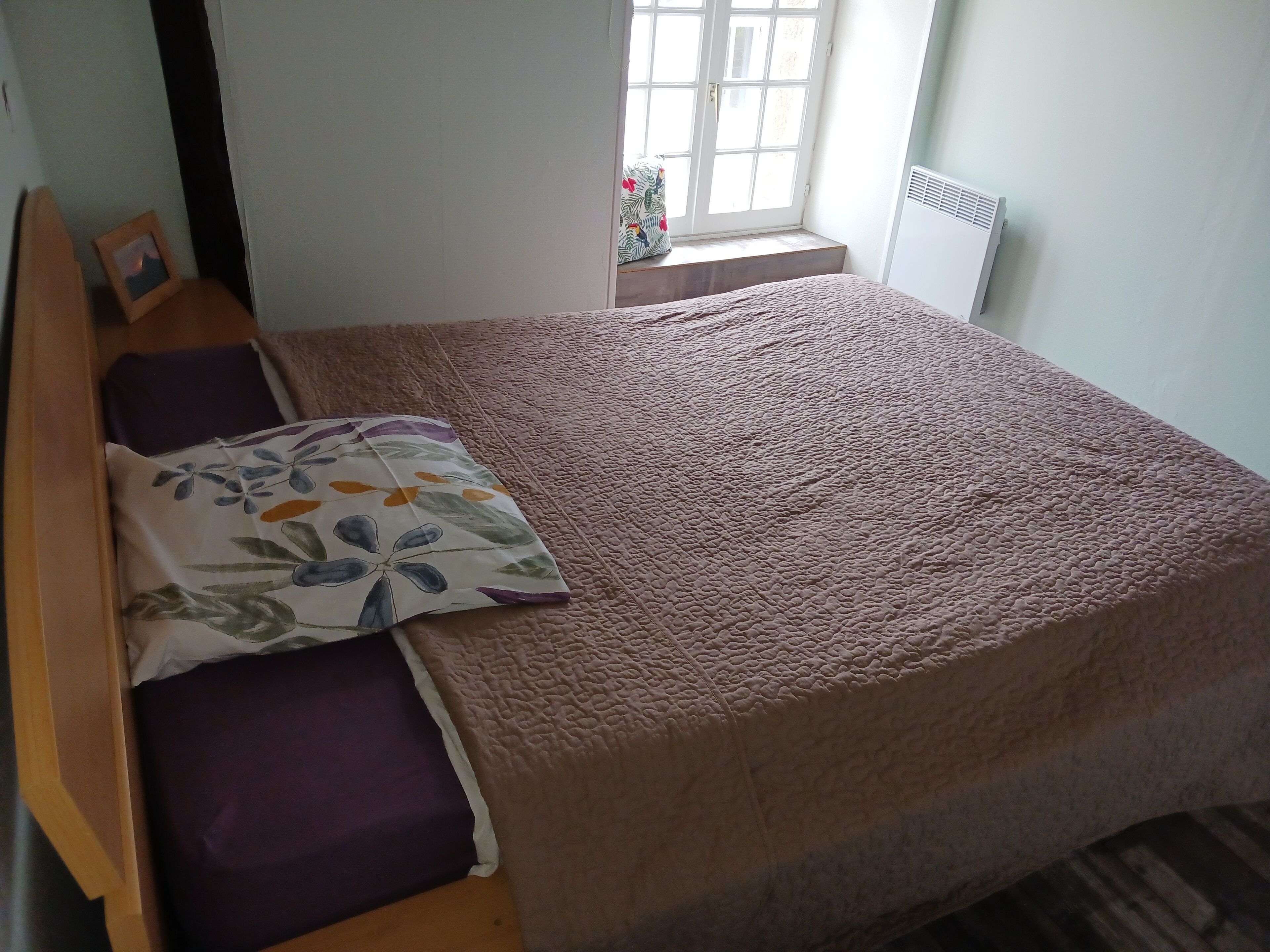 Una cama bien tendida con un cojín floral y una manta texturizada marrón.