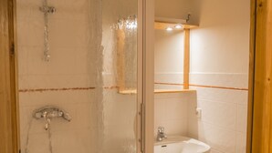 A bathroom with a glass shower enclosure, a sink, and a wooden cabinet.