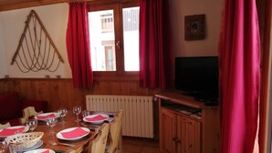 A dining area with a wooden table set for four, red napkins, and a television on a wooden stand.