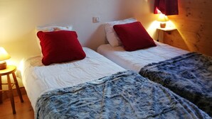A room with two beds, each with red pillows, a painting on the wall, and a window with curtains.