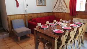 A dining area with a wooden table set for six, surrounded by wooden chairs. A red sofa and a grey armchair are positioned against the wall.