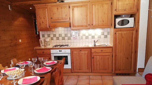 A wooden cabin-style kitchen with a dining table set for four, equipped with a gas stove, oven, and microwave.