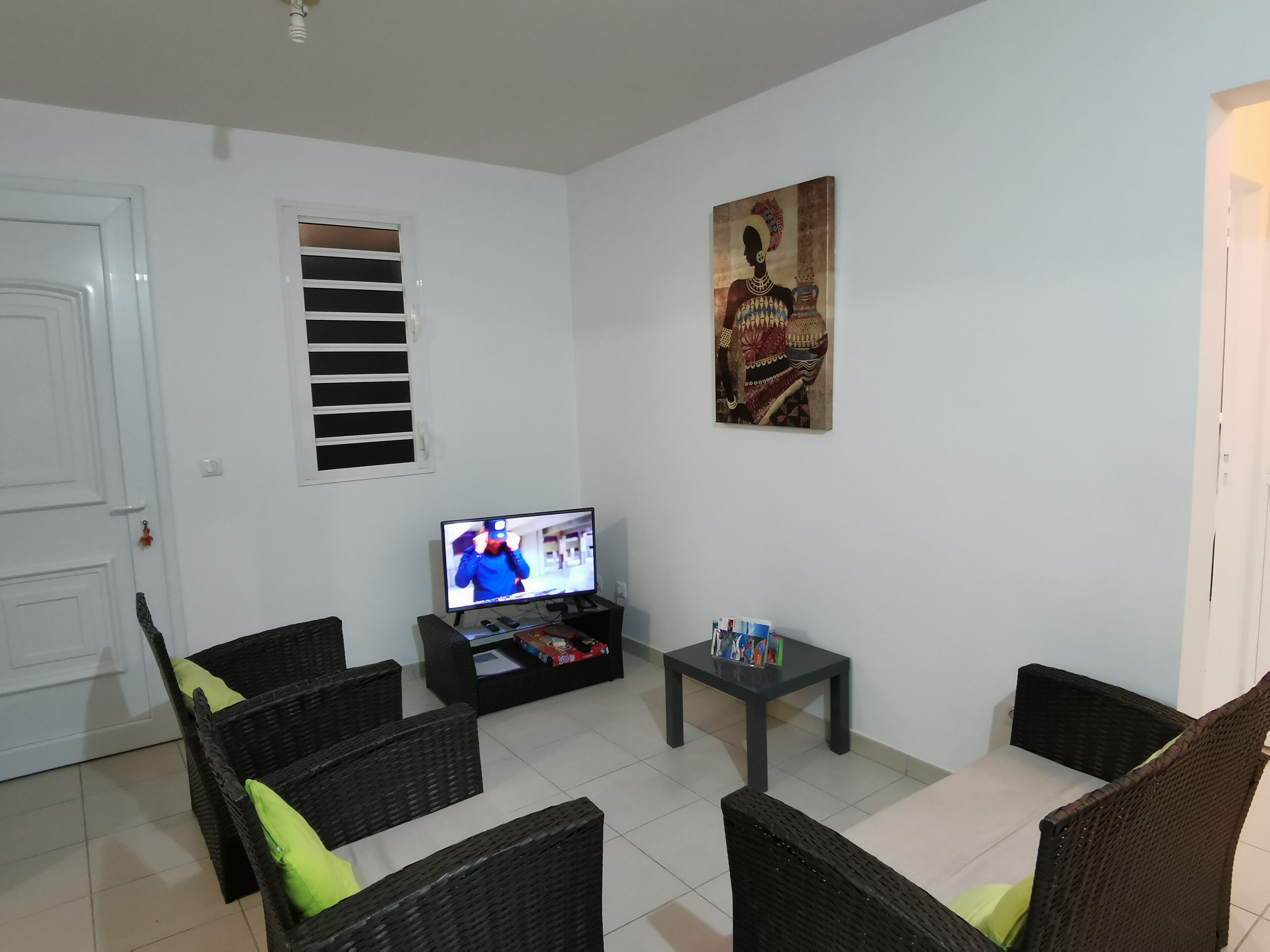 Sala de estar com móveis de vime, uma televisão, uma mesa pequena e um quadro na parede.