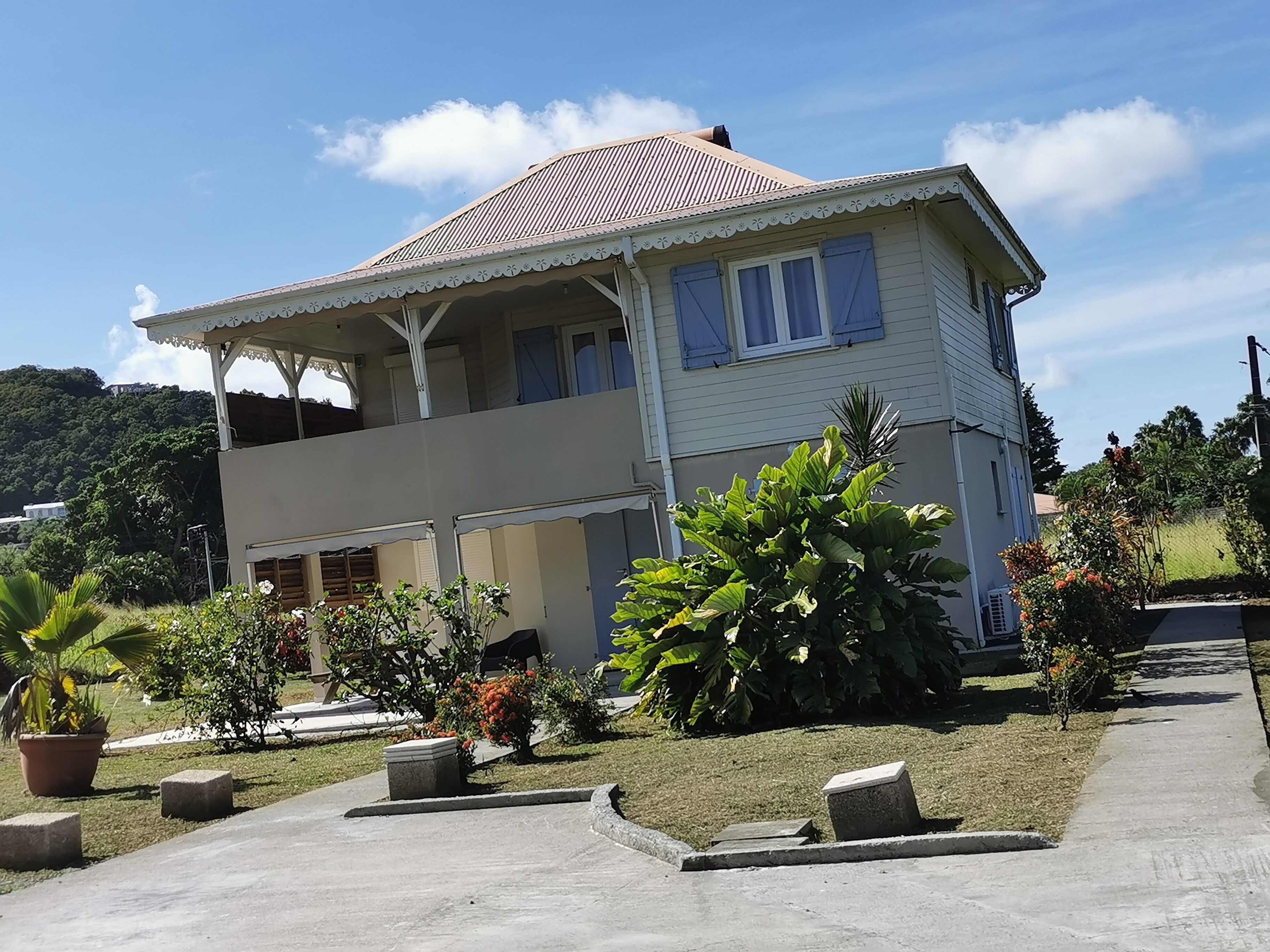 A two-story house with a balcony, surrounded by a garden with potted plants and a lawn.