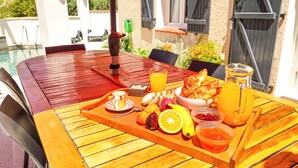 A wooden table with a breakfast tray containing fruits, croissants, and a glass of orange juice.