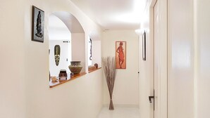 A hallway with a wooden shelf displaying decorative items, a tall vase, and framed artwork on the walls.