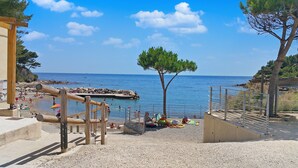A beach with a wooden swing set, a tree, and a rocky shoreline.