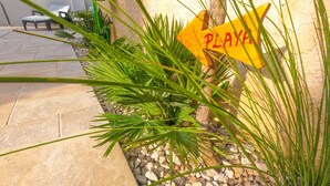 A patio area with a 'PLAYA' sign, surrounded by plants and a stone pathway.