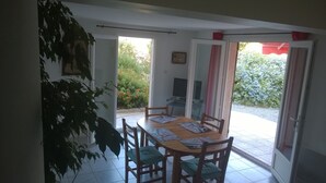 A dining area with a table and chairs, a TV, and a sliding glass door leading to a garden. - AFA villa floor 15 km from Ajaccio (Afa)