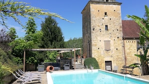 Ein Poolbereich mit einem Steinturm, Liegestühlen und einer Pergola.