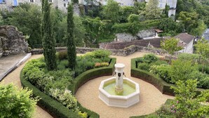 Ein historischer Innenhof mit einem zentralen Brunnen, umgeben von gepflegten Hecken und alten Steinbauten.