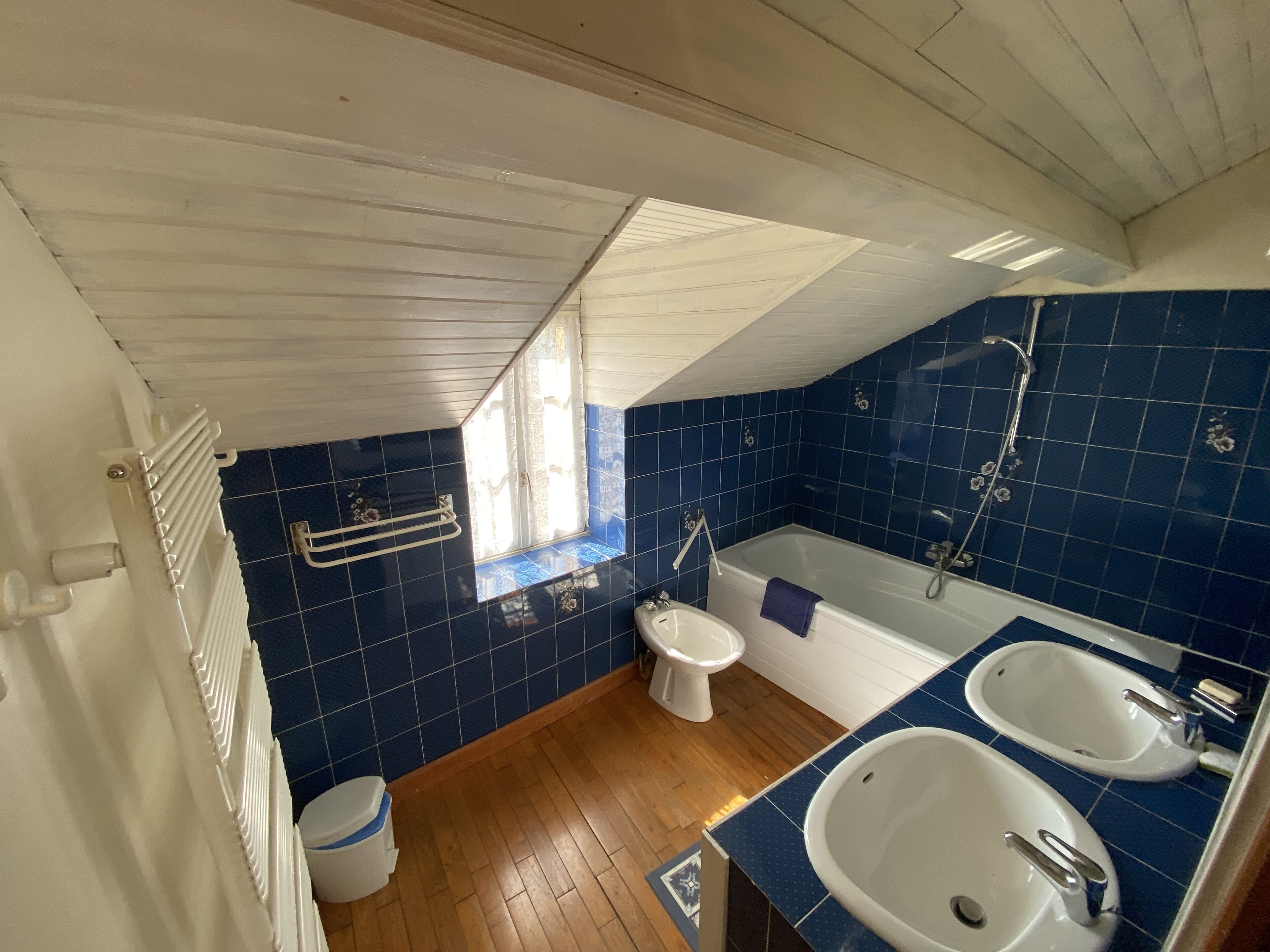 A bathroom with a wooden floor, a bathtub, two sinks, a toilet, and a window.