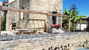 Ein Steinhaus mit einer Holzpergola, einer Steinbank und Topfpflanzen.