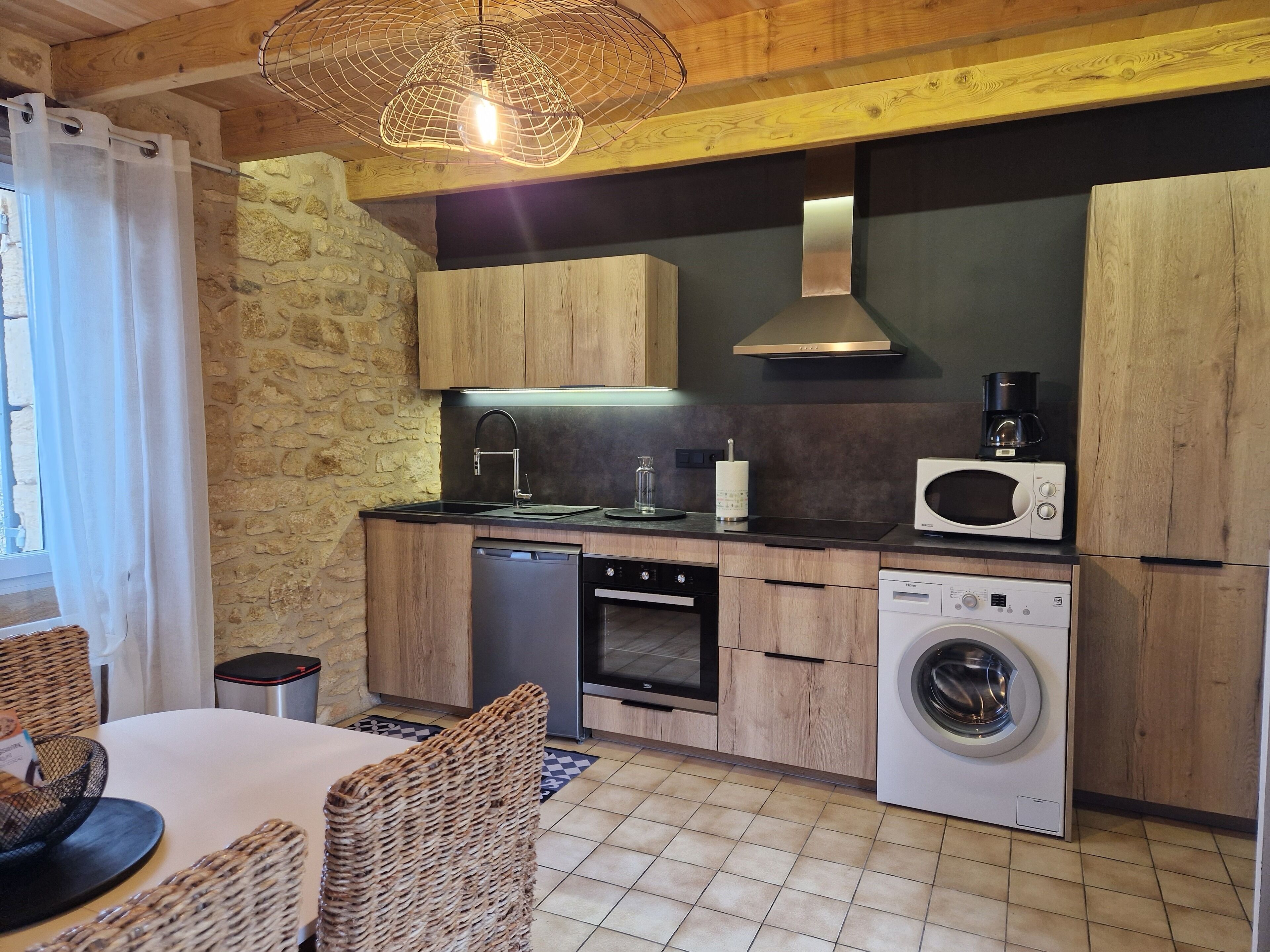 A compact kitchen with wooden cabinets, a built-in dishwasher, a washing machine, and a microwave.