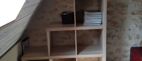 Una estantería de madera con un cuadro enmarcado encima, ubicada en una habitación con techo inclinado y pared con textura.