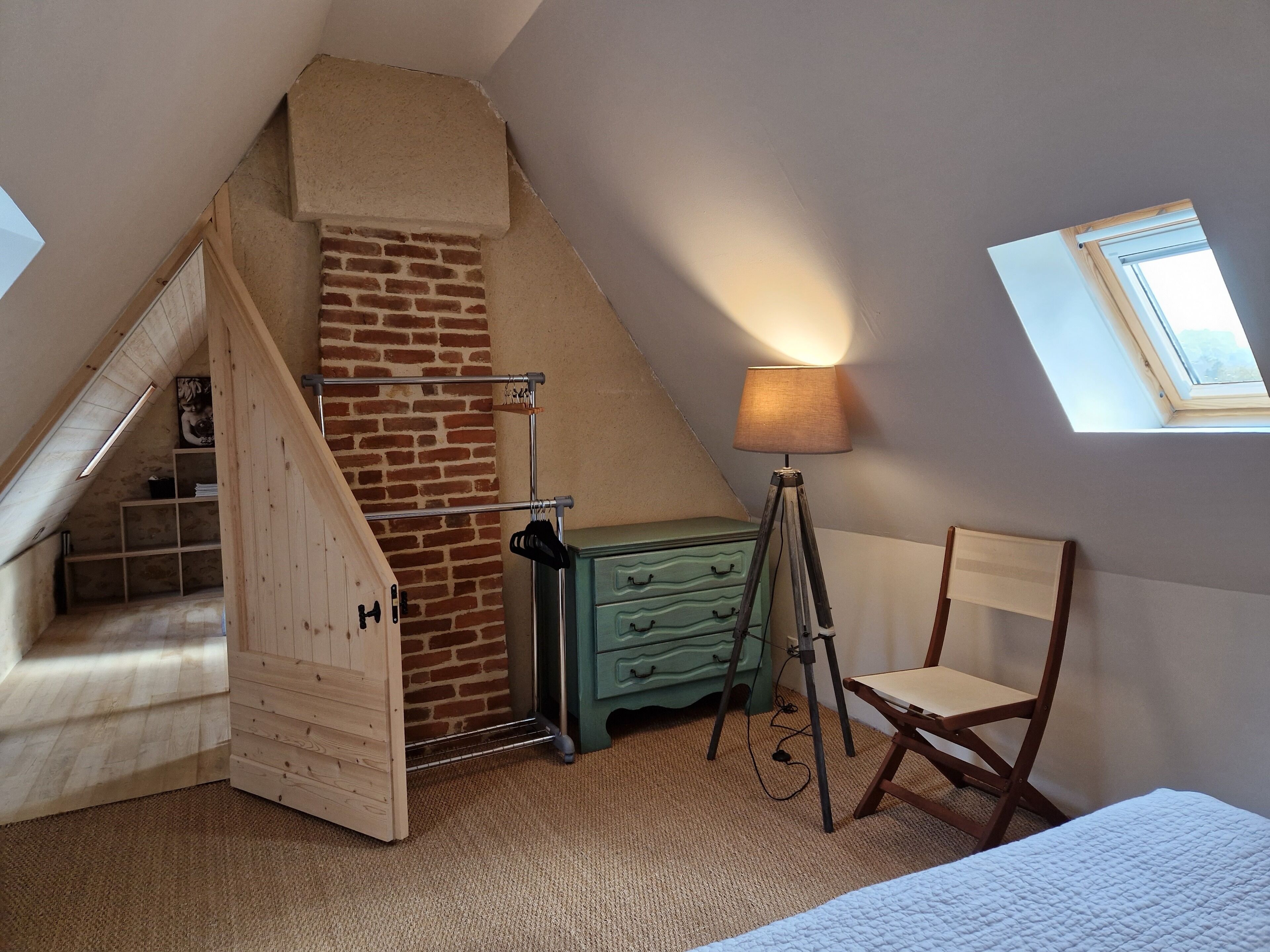 Ein gemütliches Schlafzimmer im Dachgeschoss mit schrägen Wänden, einer Holzleiter, einem grünen Schrank, einem Holzstuhl und einer Lampe.