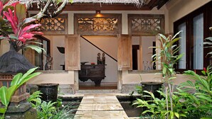 A traditional wooden structure with a thatched roof, a stone pathway leading to a water feature, and lush greenery. - Villa Ria Sayan Ubud (Ubud)