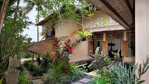 A traditional house with a thatched roof, surrounded by lush greenery and a stone pathway. - Villa Ria Sayan Ubud (Ubud)